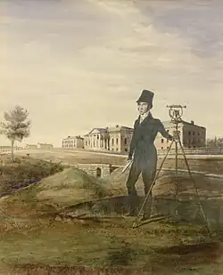 Man standing on hill beside large measuring instrument with building in background
