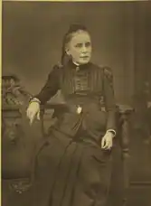 B&W portrait photo of a seated middle-aged woman wearing a dark, high-collared blouse with her hair in an up-do.