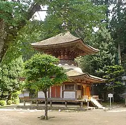 A two-storied pagoda shaped tower with a square base and a round upper story. The walls are faded white and the beams faded red.