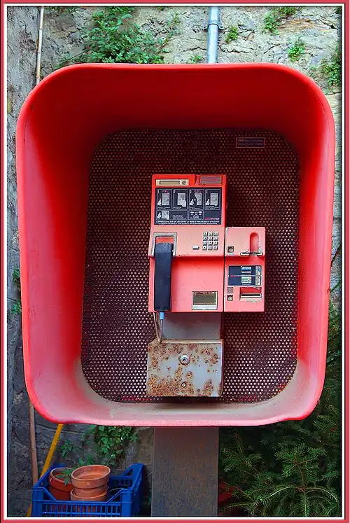Cropped view of an orange late 1980s "Rotor" public telephone pictured in an open fronted telephone booth.