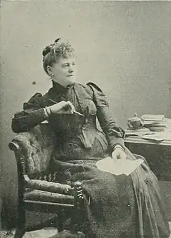 B&W photo of a seated middle-aged woman wearing a dark dress with her hair in an up-do.