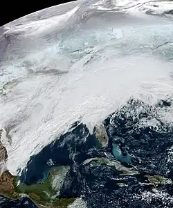 A picture of the continental United States taken from space. The Gulf of Mexico is also within view. The landscape is covered in snow and a massive white cloud system which obscures most of the continent.