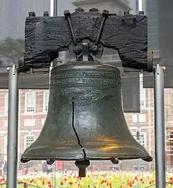 a large bronze bell with a pronounced crack in it hangs from a blackened wooden yoke