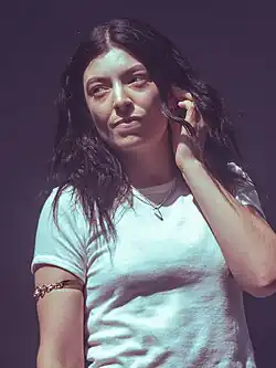 Lorde performing with one hand adjusting her earplug