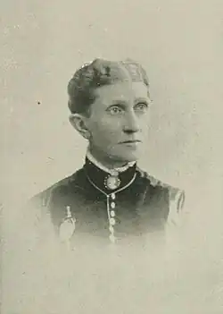19th-century B&W portrait photo of a woman with her hair in an up-do, wearing a dark, fitted blouse.