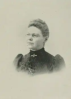 19th-century B&W portrait photo of a middle-aged white woman wearing a dark blouse with a high collar, her hair in an up-do.