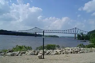 A steel cantilever-truss bridge arches gracefully over a tree-lined river.