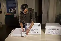 Man shown handling artifacts wrapped in white material on a table. There are two boxes with artifacts in them
