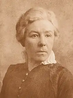 Sepia headshot of Marie Goldsmith, a woman with white hair and wearing a black dress