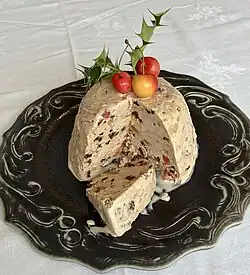 An icecream bombe topped with fresh cherries and a sprig of holly. There is dried fruit visible in the pudding, which has been turned upside down onto a serving plate and sliced open.