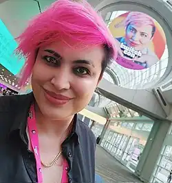 Veronica Ripley poses in front of a banner with her face on it at Twitchcon San Diego 2022