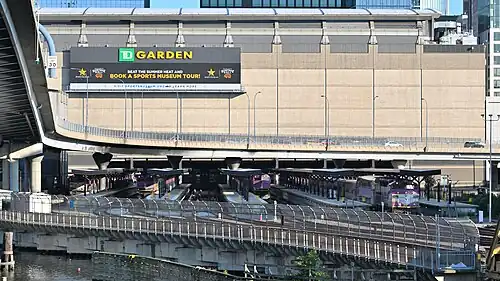 A railway station with five island platforms next to a large arena. Several passenger trains are at the platforms.