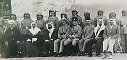 The picture shows the dignitaries of the city of Karak, its judiciary, and officials awaiting the arrival of His Highness the King of Transjordan, Abdullah I, at the train station in Qatraneh, who will arrive from the administration center in Amman. The names of the seated officials present at the Qatraneh railway station from left to right are: Sheikh Arif Tahboub al-Marwani, Mufti of Karak, then Ain Pasha al-Tarawneh, then Faydan al-Majali, then the English commander, then Bahjat Tabbara, then Mahmoud al-Bu Ghanima, Director of Karak Secondary School. The names of the other two are unknown