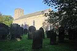 A plain stone church seen through a churchyard with a battlemented tower