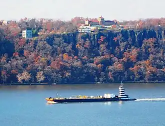 Panoramic view looking west from London Terrace. A barge on the Hudson River and the Hudson Palisades beyond, with the Englewood Cliffs campus of Saint Peter's University on the top of the Palisades