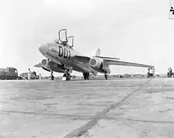 A metallic, swept-wing, combat aircraft is parked on pavement with its dual canopies raised. It is painted "Vautour 001".