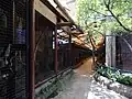 Shaded zoo walkway with mesh enclosures, trees, and monkeys nearby.