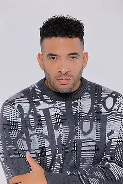 Handsome Black man with short curly hair wearing a patterned gray sweater against a light background