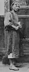 A Qing dynasty-era man carrying strings of cash coins on his shoulder in the year 1900.