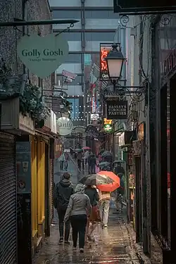 Pedestrians with umbrellas walking through Merchants' Arch, a historic laneway in the Temple Bar district of Dublin, Ireland, on a rainy day