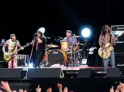 A photograph of four members of the Red Hot Chili Peppers performing on a stage