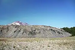 A rough-textured light-colored lava dome, with a volcanic peak behind
