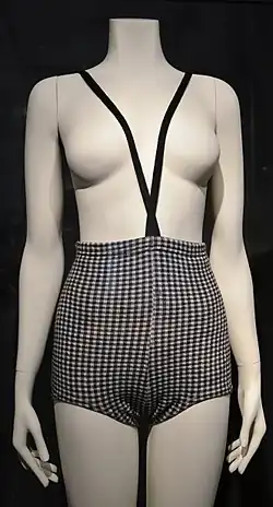 A wool monokini in a blue and white pattern, a topless one-piece swimsuit with thin straps that run between the breasts and fasten at the neck, displayed on a white mannequin.