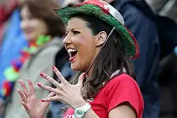 A women in Wales-flag cowboy hat, a red rugby shirt and with red painted fingernails smiles and cheers from the stand during the 2011 Rugby World Cup match between Wales and Fiji.