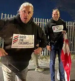 Photo of Ryan Bridge and Elliott Stanley of Raise the Colours, in Stirchley, with Ryan (left) shouting at the camera and Elliott (right) holding a flag
