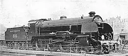 Side-and-front view of a 4-6-0 locomotive on a turntable. A member of the crew is standing next to the front.