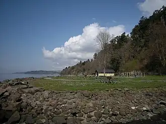 Picnic tables on a lawn surrounded by a steep rocky beach