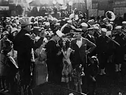 Crowd gathered around a street band with a sailor embracing a young woman in a dress at the center