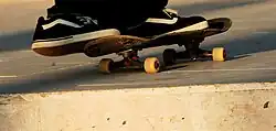 Person skateboarding wearing black and white Vans sneakers
