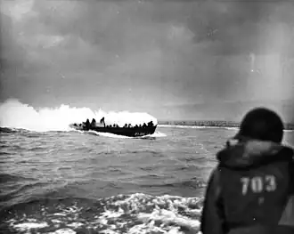 Approaching Omaha Beach, a landing craft from the Chase is drenched in smoke resulting from a German bullet hitting a smoke grenade carried by an American soldier[2]
