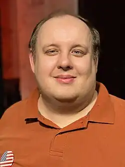 Steven Pruitt in 2022. He is a middle-aged man with dark blond hair wearing an orange collar shirt.
