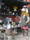 Chaiwala at a stall in Varanasi; a pot of chai is on the stove, and a tray of clean glasses is visible on the table in the background.