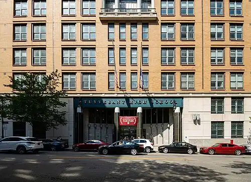 A view of the steel-and-glass main entrance to Stuyvesant High School. There is a sign above the entrance with the school's name in large capital letters.