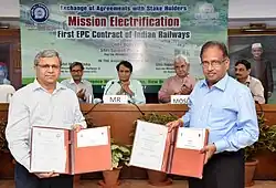 Two men present contracts side by side at an event