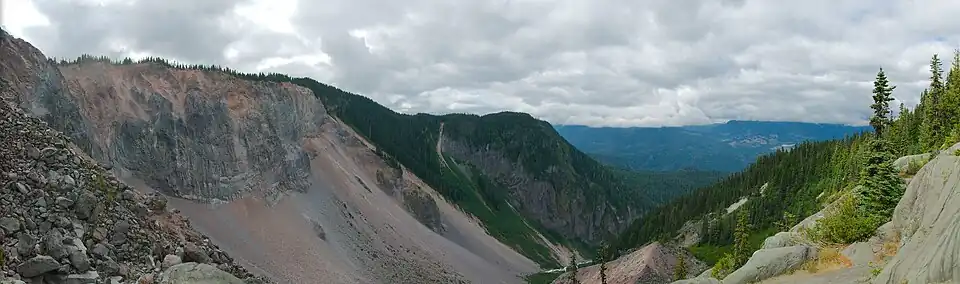 A rocky cliff rising above forest and a steep-sided rubble deposit at the base