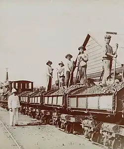 Black and white photo, circa 1920s, depicting miners on a train car bearing minerals, stopped in Thio, New Caledonia.