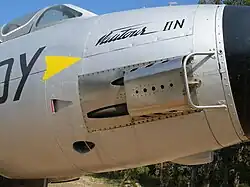 A side view of an aircraft's nose, with an apparatus partially covering 2 recessed cannon muzzles.