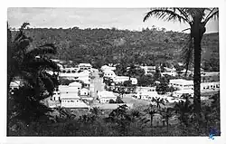 Black-and-white photograph from above showing a town with a few roads, surrounded by vegetation.