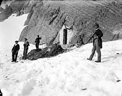 Group of men posing in front of a mountain shelter dug into the rock.