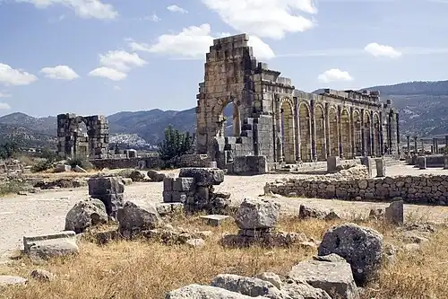Exterior view of a ruined colonnaded building of which one wall still stands