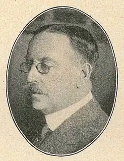 An oval portrait of a man looking to the side wearing glasses.
