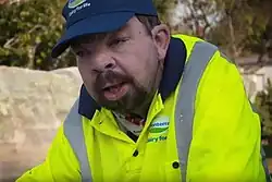 A portrait photograph of a man wearing a reflective yellow vest and blue hat with the logo of Fonterra on it.