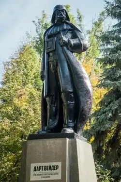 A black statue of Darth Vader with his hand on his cape. It is standing on a concrete plinth with the name of Darth Vader written on it in Ukrainian.