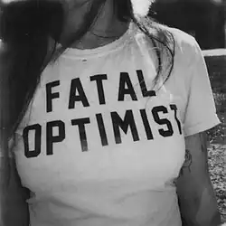 A black and white photograph zoomed in on Madi Diaz's white t-shirt, which says "Fatal Optimist".
