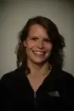 Headshot of Karen Fischer. She wears a dark top, has shoulder length wavy brown hair, and smiles at the camera.