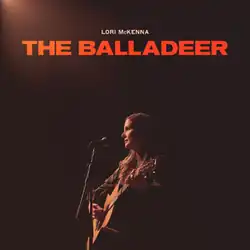 rust brown duotone photo of Lori McKenna on stage strumming guitar under title